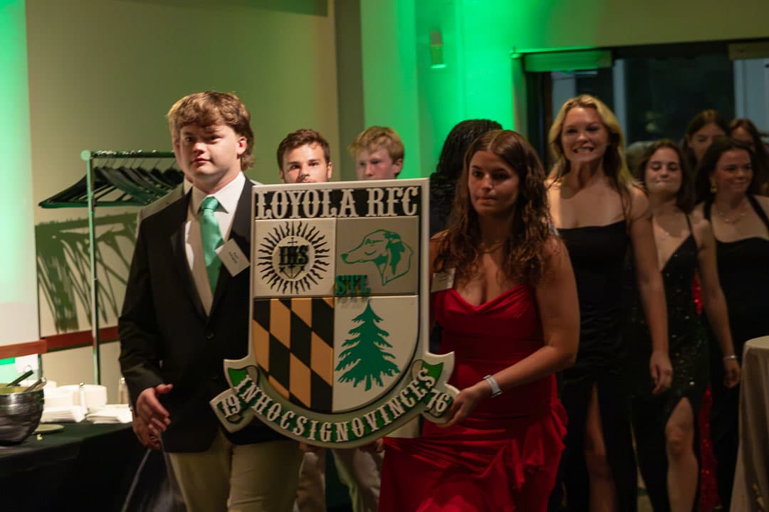 Current Loyola men's and women's players processing into McGuire Hall carrying the Loyola RFC crest